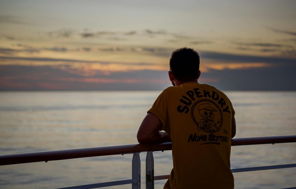 A man in a yellow t-shirt gazes at the ocean during a peaceful sunset.